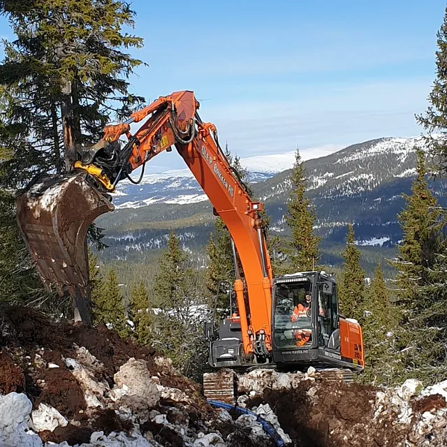 Gravemaskin i skog med rør